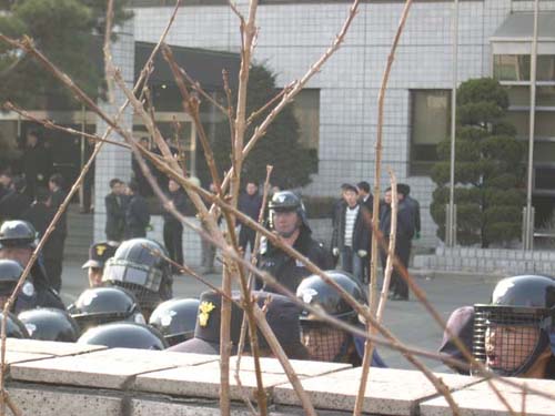 전투경찰 너머로 출입국관리소 직원들이 장갑을 끼고, 시위자들을 연행할 준비를 하고 있다. 